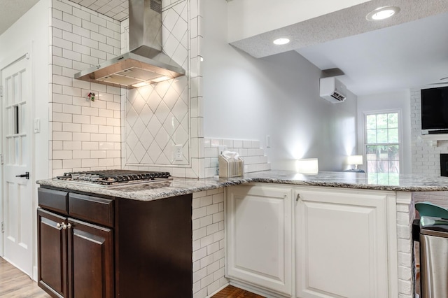 kitchen with wall chimney exhaust hood, a wall mounted AC, light stone countertops, and stainless steel gas stovetop