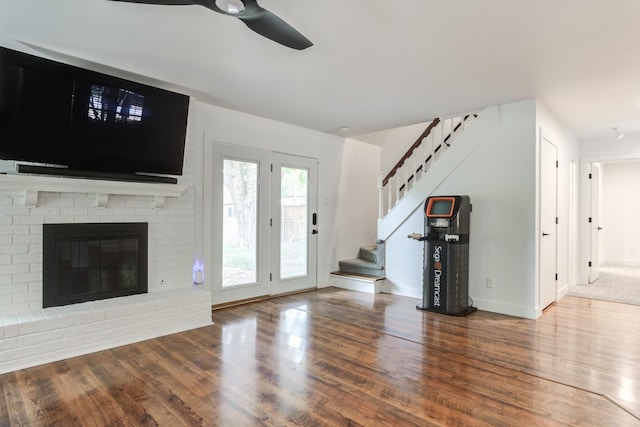 unfurnished living room with ceiling fan, a fireplace, stairway, and wood finished floors