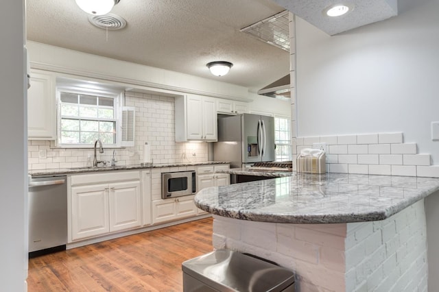 kitchen featuring appliances with stainless steel finishes, a kitchen breakfast bar, a peninsula, white cabinetry, and a sink