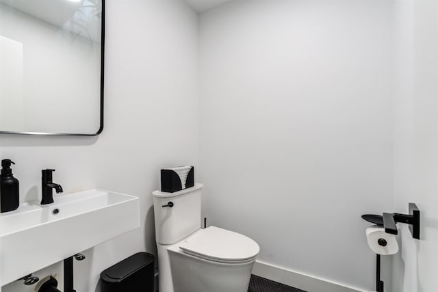 half bathroom with toilet, baseboards, and a sink