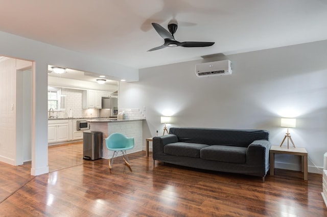 living area featuring a wall unit AC, ceiling fan, baseboards, and dark wood-type flooring