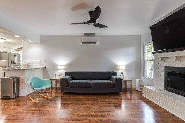 living room with a ceiling fan, a brick fireplace, a wall mounted air conditioner, and dark wood finished floors