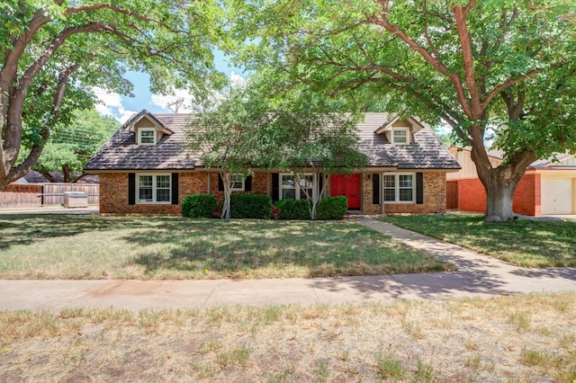 new england style home with brick siding, a front yard, and fence