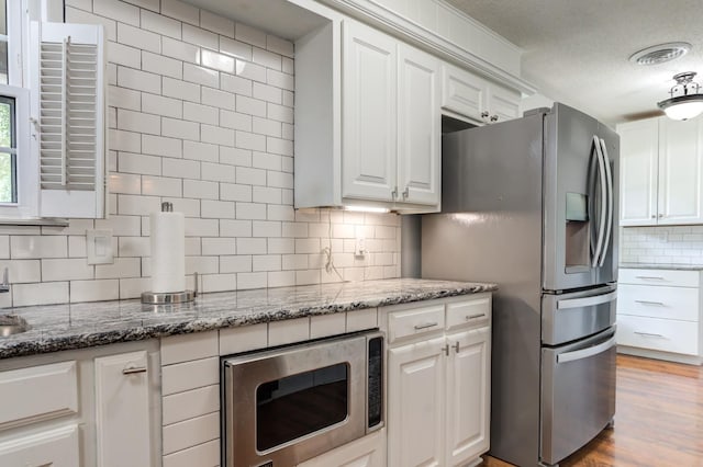 kitchen with stainless steel appliances, visible vents, backsplash, white cabinets, and dark stone counters