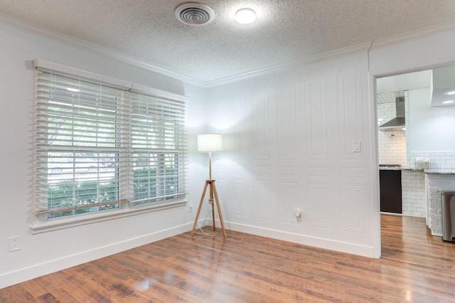 empty room featuring baseboards, wood finished floors, visible vents, and crown molding