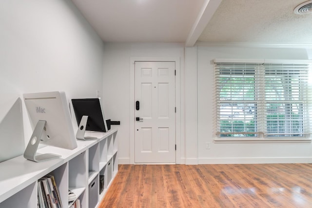 entryway featuring a textured ceiling, wood finished floors, visible vents, baseboards, and beamed ceiling