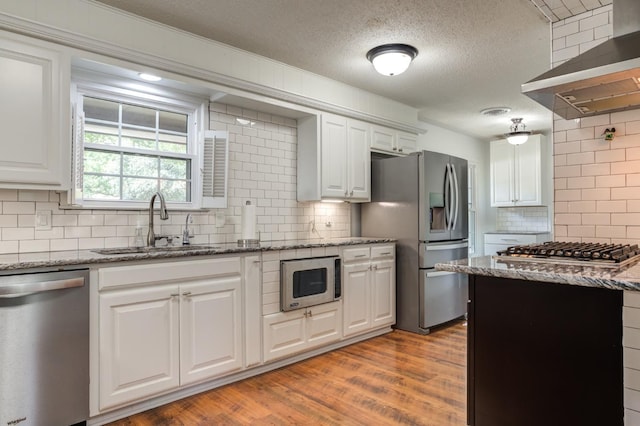 kitchen featuring wall chimney exhaust hood, a sink, white cabinets, and stainless steel appliances