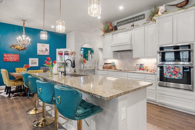 kitchen featuring dark wood-style floors, a sink, a notable chandelier, decorative backsplash, and double oven