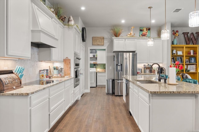 kitchen with a sink, washer / dryer, appliances with stainless steel finishes, custom exhaust hood, and white cabinetry