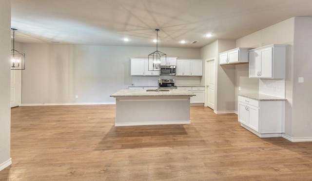 kitchen featuring decorative light fixtures, white cabinets, stainless steel appliances, light stone countertops, and a center island with sink