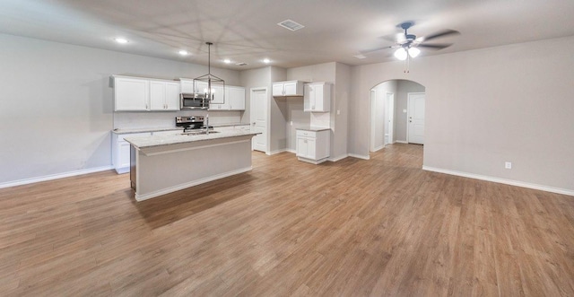 kitchen featuring white cabinetry, light stone counters, hanging light fixtures, appliances with stainless steel finishes, and a kitchen island with sink