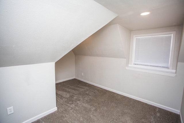 additional living space featuring lofted ceiling and dark colored carpet