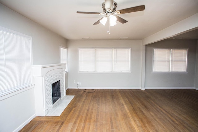 unfurnished living room featuring hardwood / wood-style flooring, ceiling fan, and a tiled fireplace