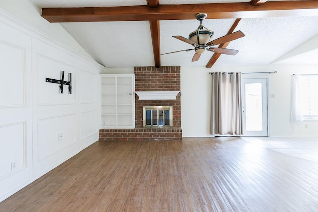 unfurnished living room featuring wood finished floors, vaulted ceiling with beams, a fireplace, and a textured ceiling