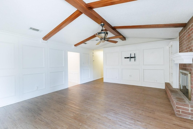 unfurnished living room with visible vents, a brick fireplace, lofted ceiling with beams, wood finished floors, and a decorative wall