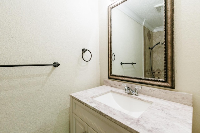 bathroom with vanity, visible vents, a textured ceiling, crown molding, and a textured wall