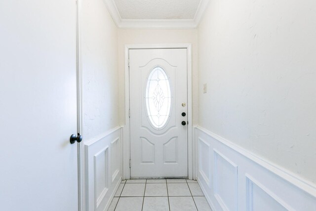 doorway with a wainscoted wall, ornamental molding, a textured ceiling, a decorative wall, and light tile patterned floors