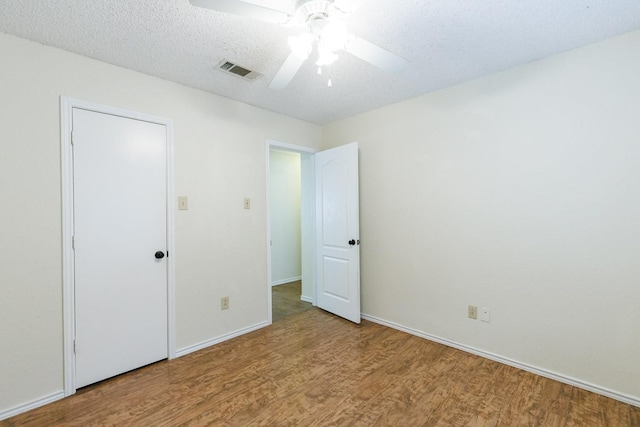 unfurnished bedroom featuring a ceiling fan, baseboards, wood finished floors, visible vents, and a textured ceiling