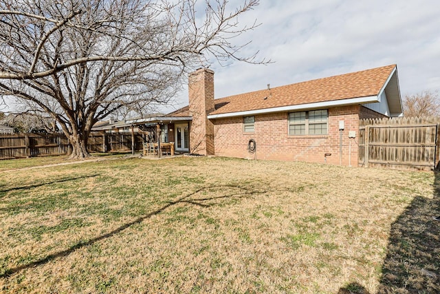 rear view of house with brick siding, a lawn, a chimney, a fenced backyard, and a patio