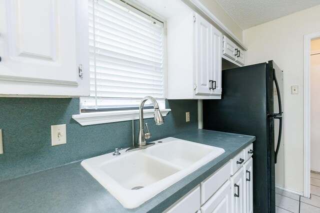 kitchen featuring white cabinetry, sink, black refrigerator, and a textured ceiling