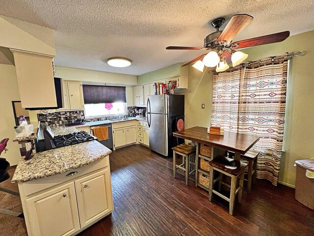 kitchen with appliances with stainless steel finishes, backsplash, ceiling fan, light stone counters, and dark wood-type flooring