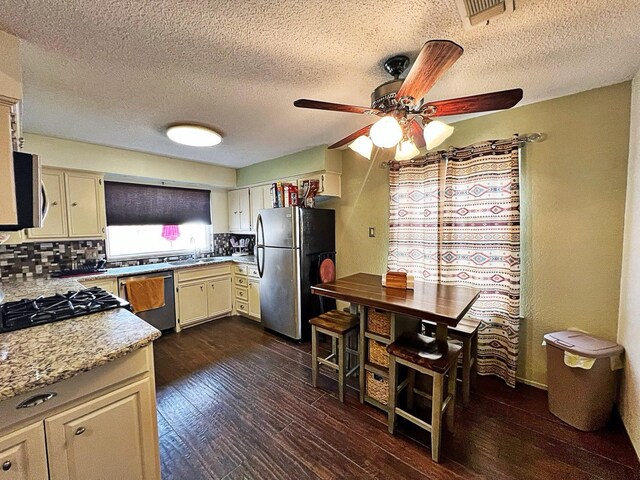 kitchen with dark wood-type flooring, sink, light stone counters, appliances with stainless steel finishes, and decorative backsplash