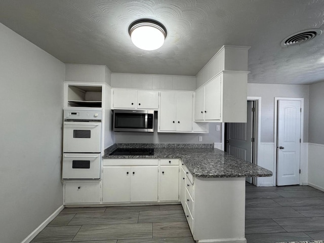 kitchen featuring white cabinetry, white double oven, black electric stovetop, and dark stone countertops