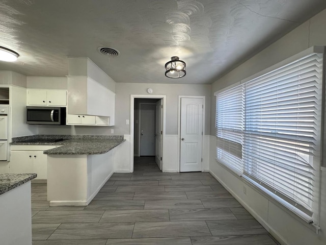 kitchen with white cabinetry, dark stone counters, and a textured ceiling