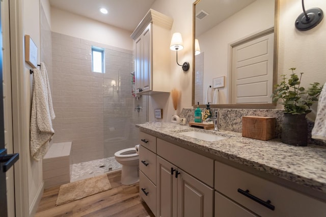 bathroom with vanity, toilet, hardwood / wood-style floors, and a tile shower