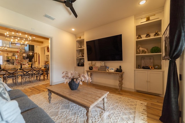 living room with ceiling fan with notable chandelier, light wood-type flooring, and built in shelves