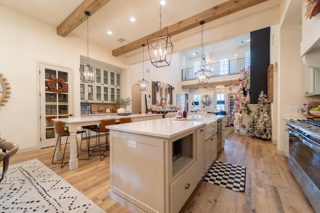 kitchen featuring stainless steel stove, an inviting chandelier, hanging light fixtures, beam ceiling, and a spacious island