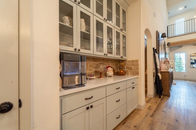 kitchen featuring tasteful backsplash, light hardwood / wood-style floors, a high ceiling, and white cabinets