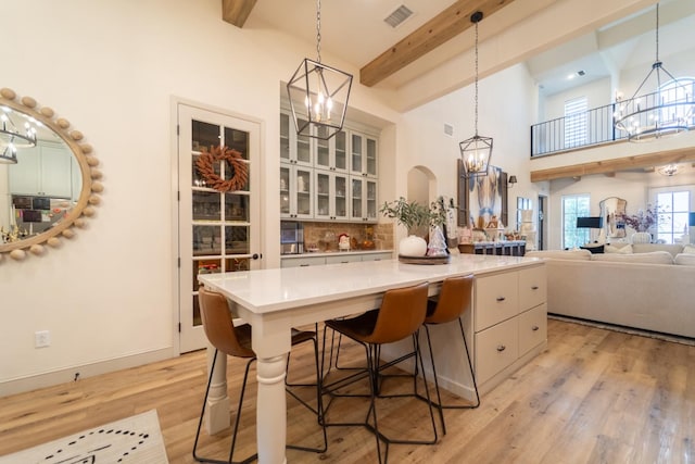 kitchen with hanging light fixtures, light wood-type flooring, an inviting chandelier, and beamed ceiling