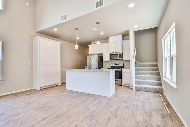 kitchen with stainless steel appliances, white cabinetry, hanging light fixtures, and a center island with sink