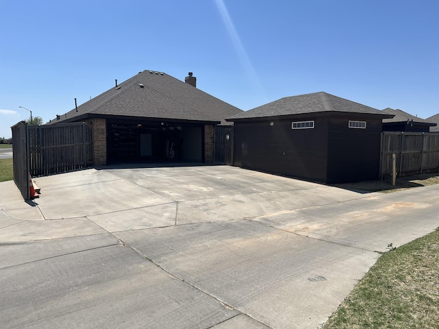 exterior space with fence, roof with shingles, concrete driveway, and brick siding