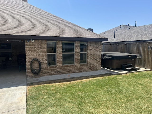 exterior space featuring a patio, a hot tub, roof with shingles, a yard, and brick siding