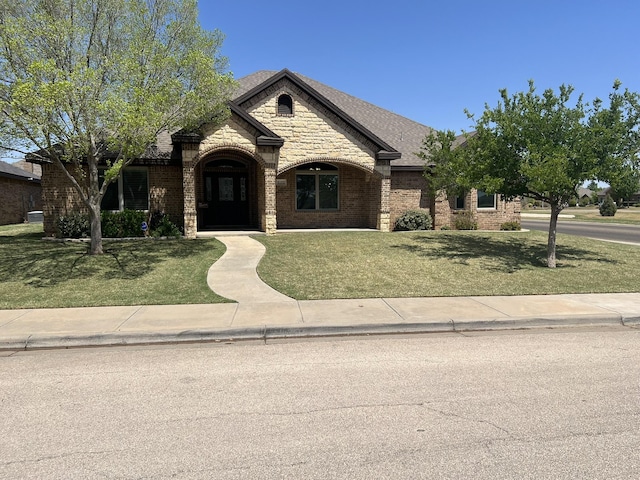 french provincial home featuring a front yard, brick siding, and stone siding