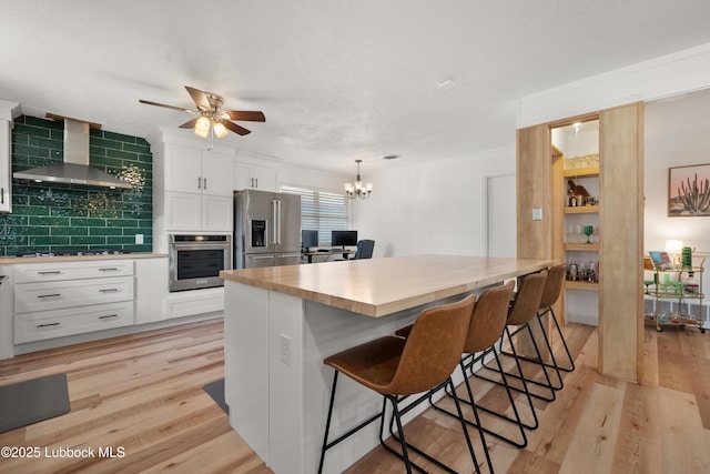 6405 Joliet Ave, Lubbock, TX 79413 - kitchen featuring stainless steel appliances, wall chimney exhaust hood, white cabinetry, light wood-style floors, and a ceiling fan