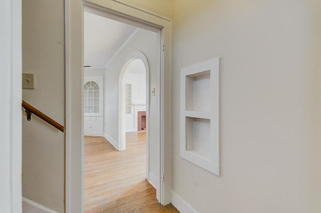 hall with ornamental molding, built in features, and light hardwood / wood-style flooring