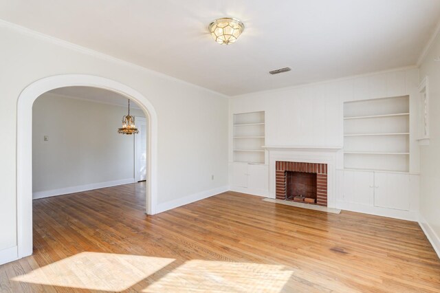 unfurnished living room with a brick fireplace, hardwood / wood-style flooring, ornamental molding, and built in features