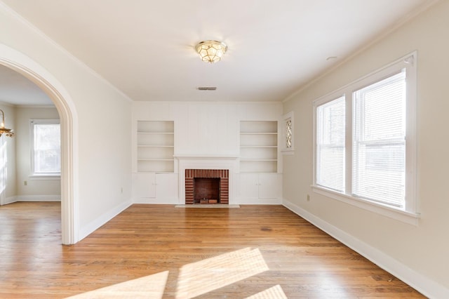 unfurnished living room with ornamental molding, a brick fireplace, built in features, and light wood-type flooring