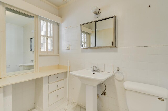 bathroom with ornamental molding, toilet, sink, and tile walls