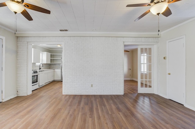 unfurnished living room with sink, ornamental molding, hardwood / wood-style floors, and brick wall