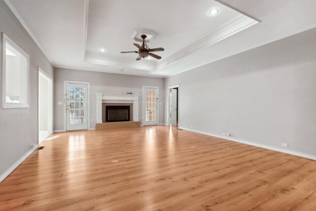 unfurnished living room featuring a tray ceiling, a fireplace, ceiling fan, light hardwood / wood-style floors, and crown molding