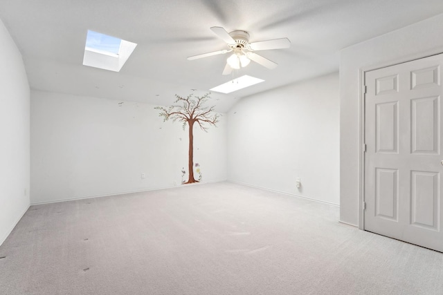 carpeted empty room with vaulted ceiling with skylight and ceiling fan