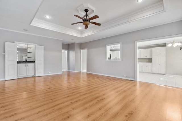 unfurnished living room featuring crown molding, ceiling fan with notable chandelier, a raised ceiling, and light wood-type flooring