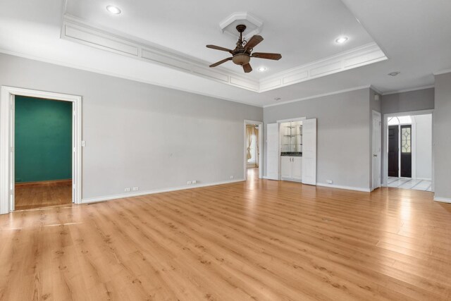 unfurnished room with ornamental molding, light wood-type flooring, ceiling fan, and a tray ceiling