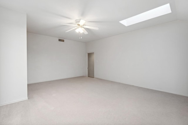 carpeted empty room with vaulted ceiling with skylight and ceiling fan