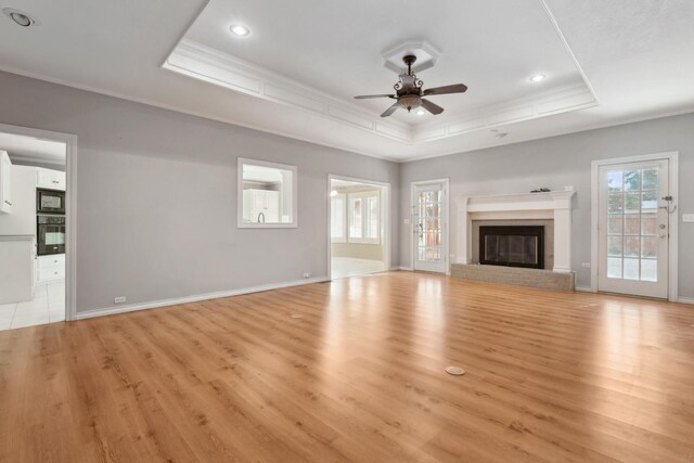 unfurnished living room with ornamental molding, a tray ceiling, and light wood-type flooring