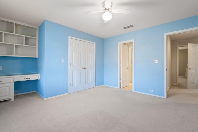 unfurnished bedroom with ceiling fan, light colored carpet, built in desk, and a closet